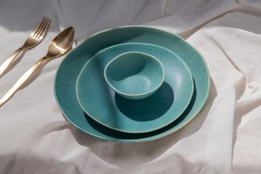 Set of Ceramic Plates with Brass cutlery on white textured table cloth. Ceramic tableware, Beautiful arrangement.