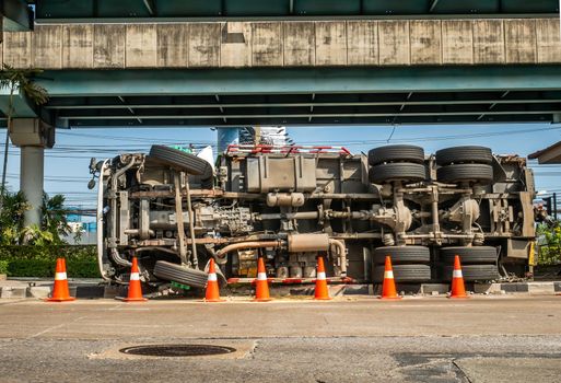 A view of under the truck carrying a container overturned on a road under a bridge over an intersection.
