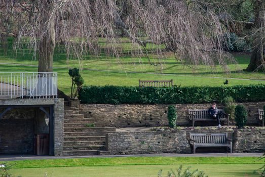 Guildford, United Kingdom - May 05, 2019 : A man sit and relax on wooden bench in Guildford Castle and Grounds. Focus and blur.