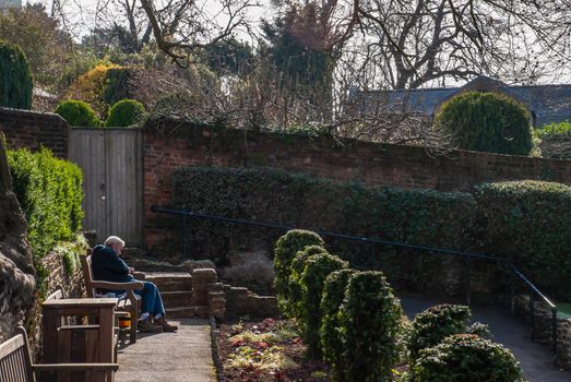 Guildford, United Kingdom - May 05, 2019 : Elderly man relaxing on wooden bench in park. No focus, specifically.