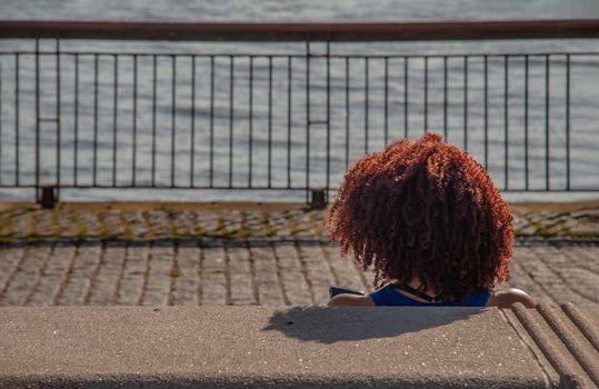 The back of the Afro hairstyle woman's head sitting and relax by the river with copy space. Fashionable youth hairstyle from red hair on the girl's head. No focus, specifically.