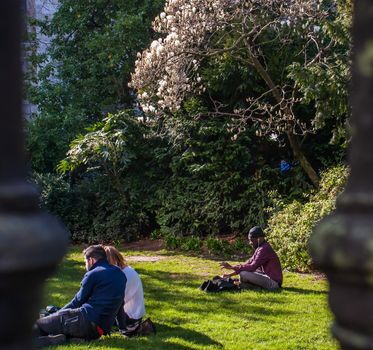 London, United Kingdom - APR 21, 2019 : Young people sit and relax on a green lawn in a park. Summer afternoon in the park. No focus, specifically.