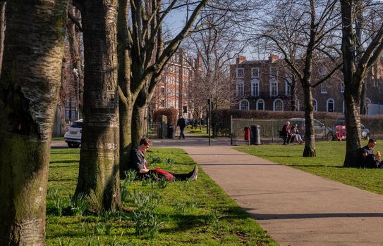 London, United Kingdom - Feb 24, 2019 : People sit and relax on a green lawn in a park. Summer afternoon in the park. No focus, specifically.