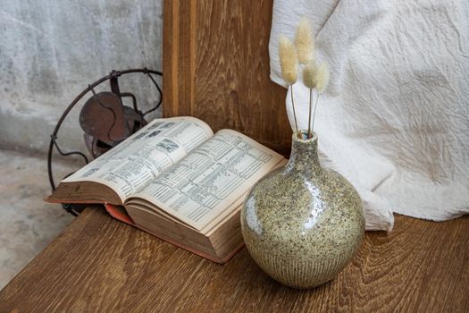 Dried flowers in handmade ceramic vases and book on wooden background. Home decoration, space for text.
