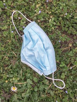 Surgical face mask abandoned on the ground into grass. Coronavirus covid-19 pandemic.