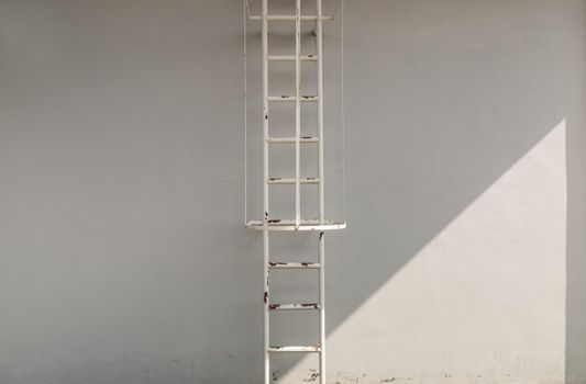 White metal fire escape attached to a wall and leading to the roof of a building. Copy space, Selective focus.