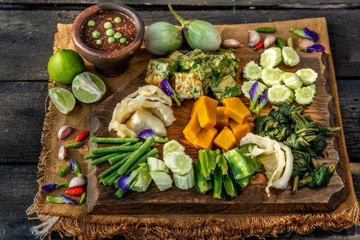 Thai Traditional Local Food : Spicy Shrimp Paste Dip or Fried shrimp paste sauce (Nam Prik Kapi) with blanched vegetables and cha-om omelets on wooden backgroud.
