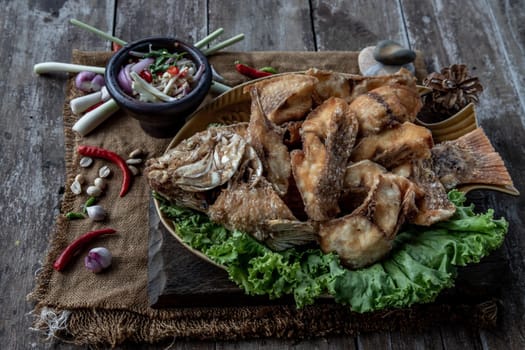Deep fried Tubtim fish with fish sauce on vintage wooden, The perfect frying process, Set hot fire, then bring the Tubtim fish to fry to frame and topped with fish sauce.