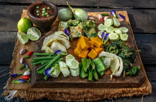Thai Traditional Local Food : Spicy Shrimp Paste Dip or Fried shrimp paste sauce (Nam Prik Kapi) with blanched vegetables and cha-om omelets on wooden backgroud.