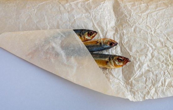 A smoked horse mackerel close-up lies wrapped on a crumpled paper background .