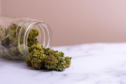 A Glass Mason Jar With Green and Orange Cannabis Nugs Pouring Out of It on a Granite Counter Background