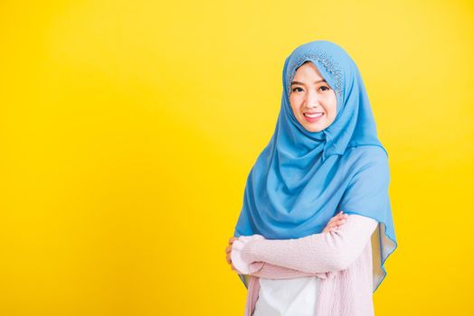 Asian Muslim Arab, Portrait of happy beautiful young woman Islamic religious wear veil hijab she smiling stand crossed arm, studio shot isolated on yellow background