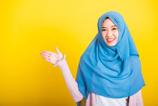 Asian Muslim Arab, Portrait of happy beautiful young woman Islam religious wear veil hijab funny smile she positive expression open palms with something on hand side space isolated yellow background