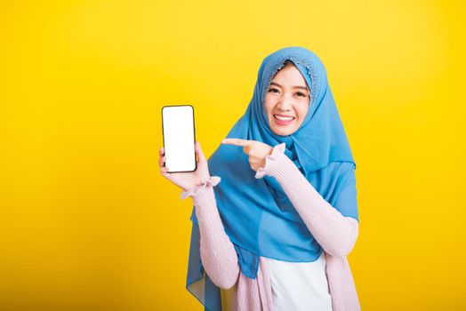 Asian Muslim Arab, Portrait of happy beautiful young woman Islam religious wear veil hijab funny smile she showing blank screen smart mobile phone and point screen isolated on yellow background