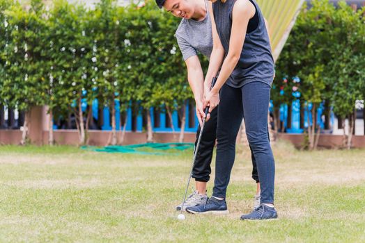 Asian young man support teaching training woman to play perfect golf while standing together in nature a field garden park. Couple trainer giving a lesson on the golf course