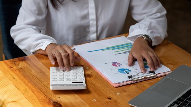 Close up of businessman or accountant hand holding pen working on calculator to calculate business data, accountancy document and laptop computer at office, business concept