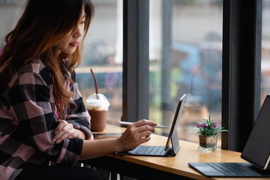 Young creative designer holding stylus pen drawing on screen of digital tablet at cafe.