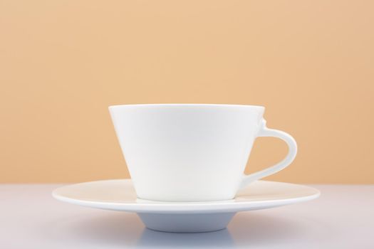 Selective focus, close up of white porcelain coffee or tea cup on white table against beige background. Concept of hot drinks and kitchenware