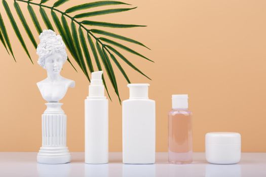 Set of skin care products with gypsum figure of a woman on white table against beige background with palm leaf. Face cream, lotion, tonic and under eye gel. Products for daily skin care