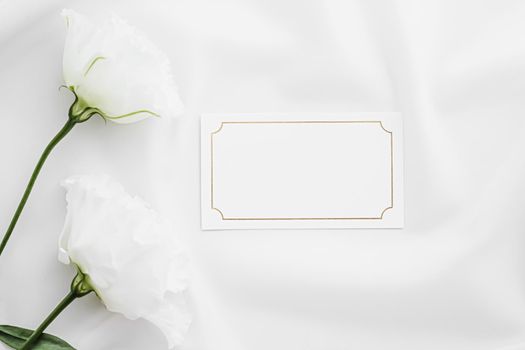 Wedding invitation or gift card and white rose flowers on silk fabric as bridal flatlay background, blank paper and holiday branding, flat lay design concept