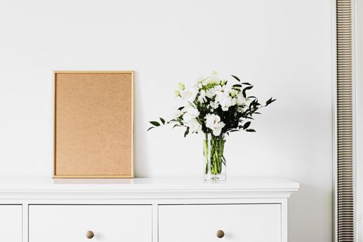 Golden vertical frame and bouquet of fresh flowers on white furniture, luxury home decor and design for mockup creations