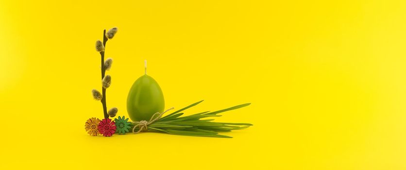 Minimalistic style Easter banner with egg shaped candle, pussy willow branch and bundle of wheat seedlings on yellow background with free copy space for your text