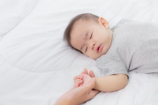 Young asian mother touch hand of little baby girl with tender on bed in the bedroom, mom love newborn and care, woman with expression with child together, parent and daughter, family concept.
