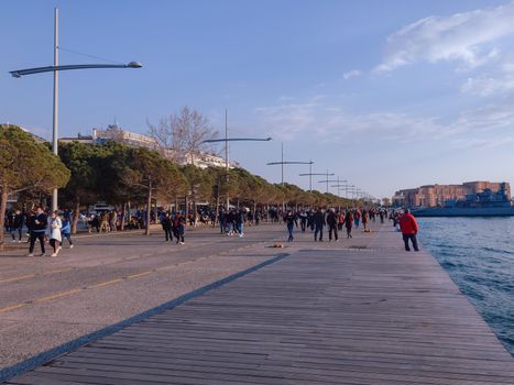 Unidentified crowd with face protection walks at close distance on city waterfront.