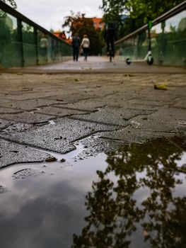 Small puddle in front of long wooden bridge with walking people