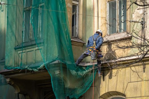 repair of the facade of the house by a man on suspension ropes.