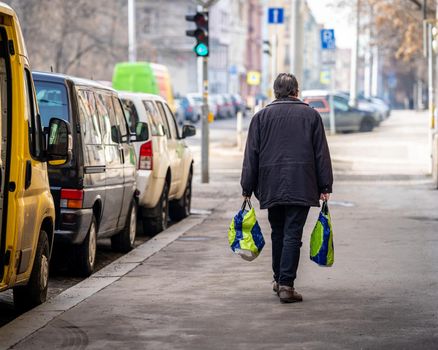 man walks down the street with purchases in plastic bags.