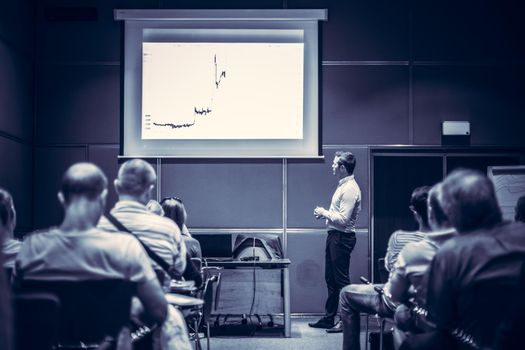 Speaker giving a talk in conference hall at business event. Unrecognizable people in audience at conference hall. Business and Entrepreneurship concept. Blue toned black and white.