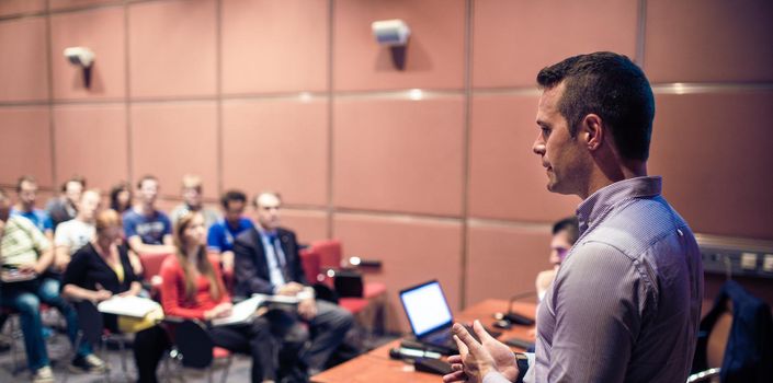 Speaker giving a talk on corporate business conference. Unrecognizable people in audience at conference hall. Business and Entrepreneurship event.