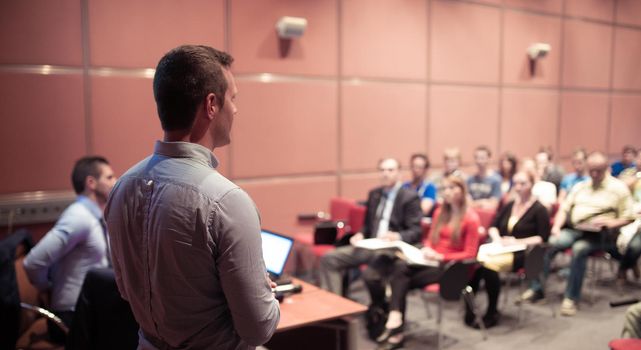 Speaker giving a talk on corporate business conference. Unrecognizable people in audience at conference hall. Business and Entrepreneurship event.