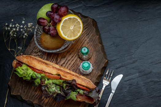 A delicious Smoked salmon sesame bread sandwich with Fresh fruit on a wooden plate. It is perfect eaten with salads and flavoursome cheeses. Healthy breakfast food. Top view. Place for text.