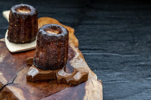 Cannelés (Canelés) de Bordeaux Recipe is a small pastry with rum and vanilla on a wooden plate. Traditional French sweet dessert. tasty snacks. Oblique view from the top. Place for text.