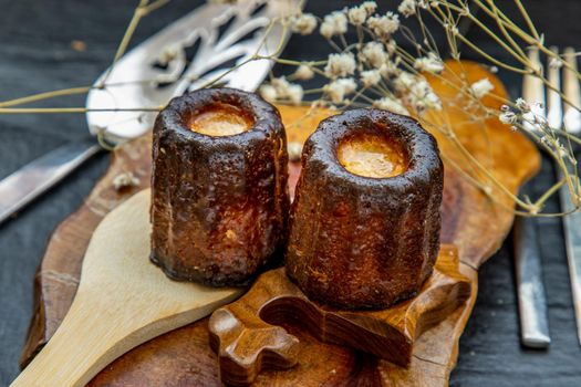 Cannelés (Canelés) de Bordeaux Recipe is a small pastry with rum and vanilla on a wooden plate. Traditional French sweet dessert. tasty snacks. Oblique view from the top.
