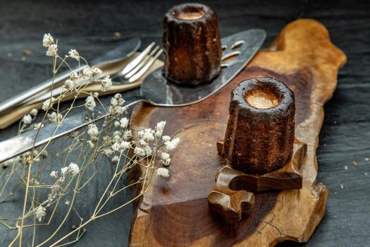 Cannelés (Canelés) de Bordeaux Recipe is a small pastry with rum and vanilla on a wooden plate. Traditional French sweet dessert. tasty snacks. Oblique view from the top.