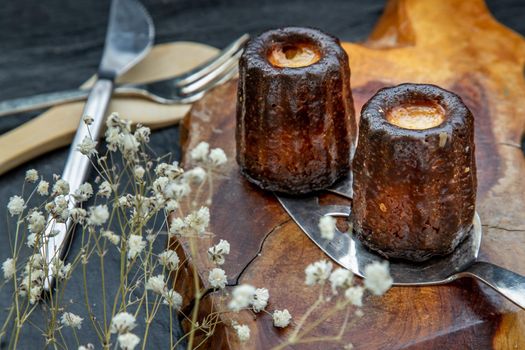 Cannelés (Canelés) de Bordeaux Recipe is a small pastry with rum and vanilla on a wooden plate. Traditional French sweet dessert. tasty snacks. Oblique view from the top.