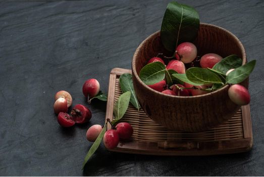 Bengal-Currants, Carandas-plum or Karonda fruit (Carissa carandas L.) sour taste fruit in Wooden cup on wicker. Oblique view from the top.