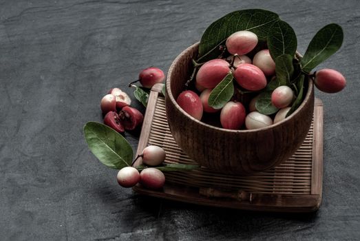 Bengal-Currants, Carandas-plum or Karonda fruit (Carissa carandas L.) sour taste fruit in Wooden cup on wicker. Oblique view from the top.
