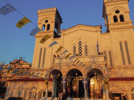 Evening view of unidentified crowd with face protection outside an Orthodox church with Greek and Byzantine flags.