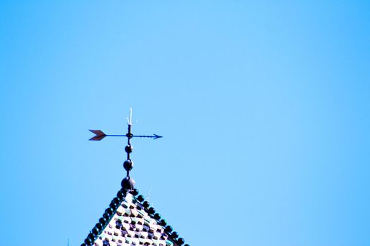 Weather vane above house with blue sky background. Copy space