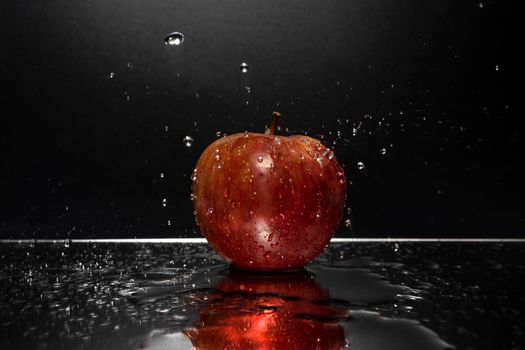 A red apple resting on a mirror with falling water drops