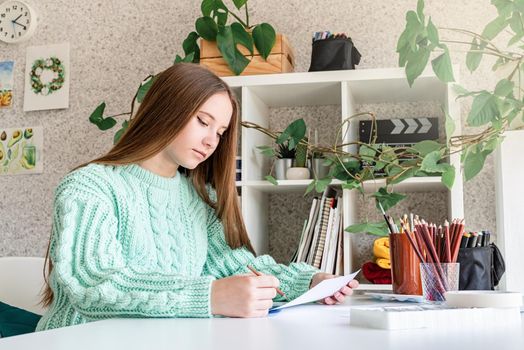 Young woman artist in mint green sweater holding color palette working at home