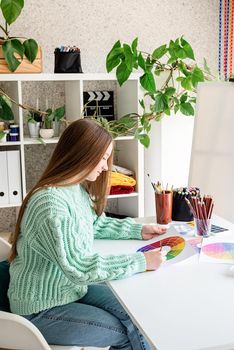 Young woman artist in mint green sweater holding color palette working at home