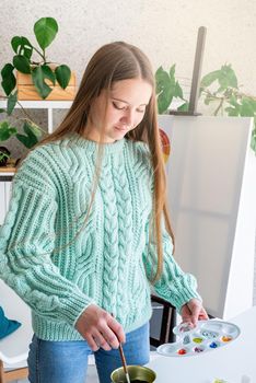 Young woman artist in mint green sweater holding color palette working at home