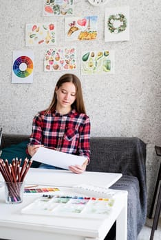 Young woman artist in check shirt painting a picture at home