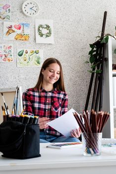 Young woman artist in check shirt painting a picture at home