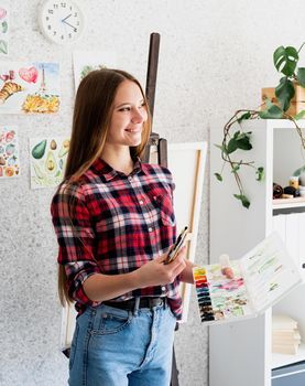 Young woman artist in check shirt painting a picture at home